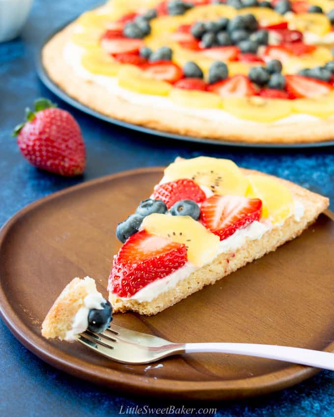 A slice of fruit pizza on a wooden place with a piece on a fork.