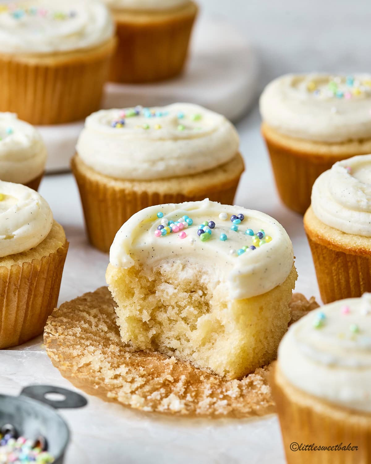 Vanilla cupcakes topped with vanilla buttercream with one missing a bite.