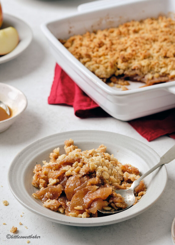 A bowl of apple crisp with the rest of the apple crisp in the background.