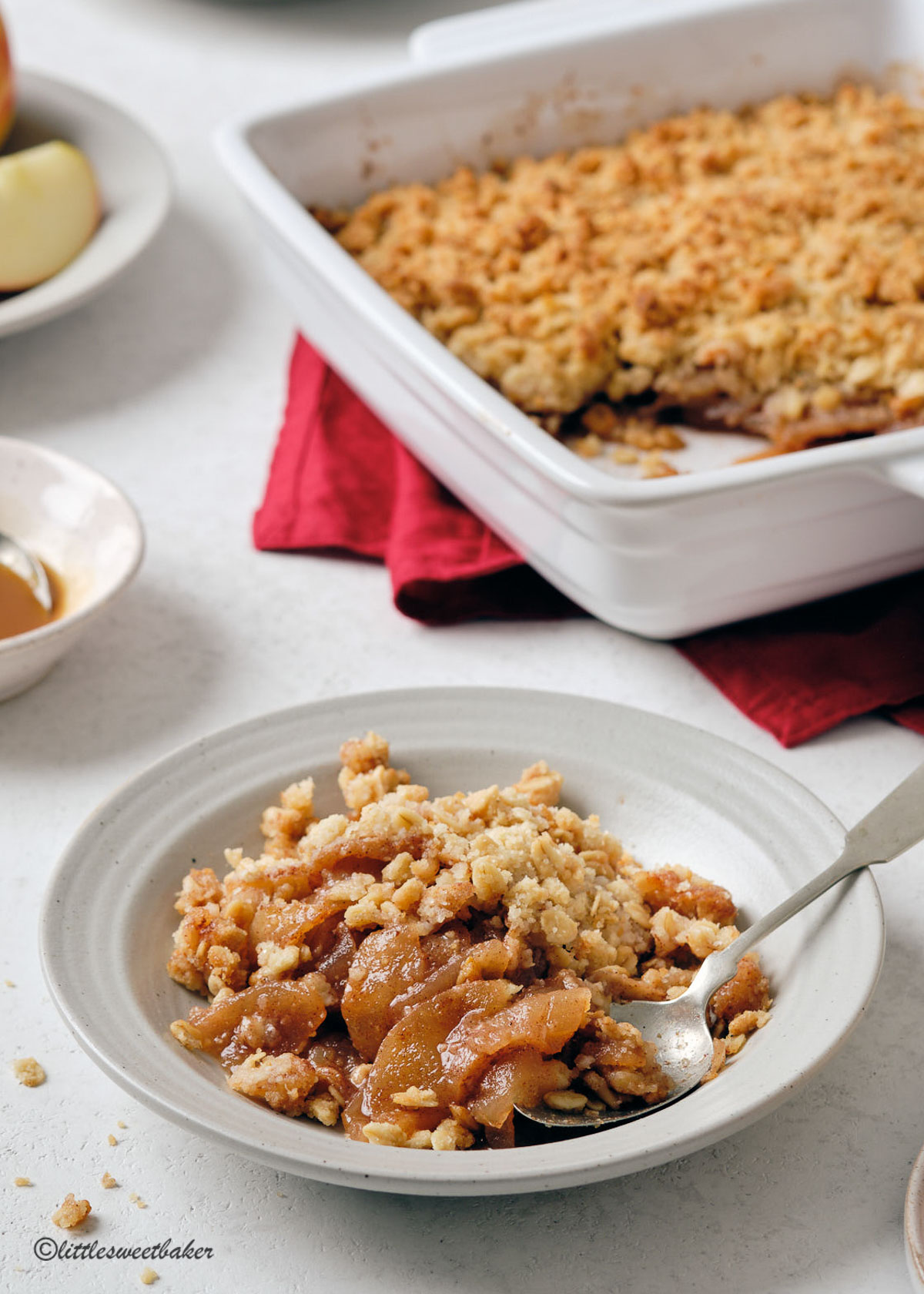 A bowl of apple crisp with the rest of the dish in the background