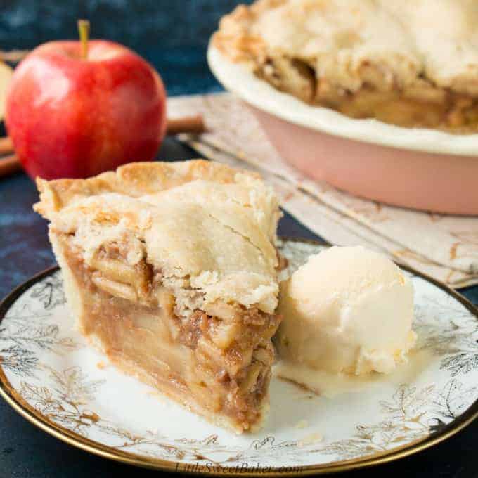 A slice of apple pie with ice cream on a white and gold plate.