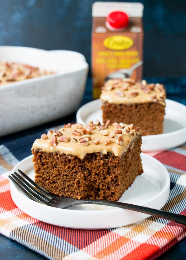 A slice of glazed gingerbread cake with a piece missing on a white plate with a dark fork.