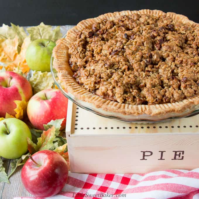 An apple crumble pie on top of a pie box surrounded by apples.