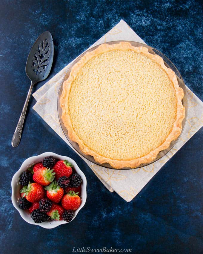 A whole buttermilk pie on a napkin with a bowl of berries and cake server.