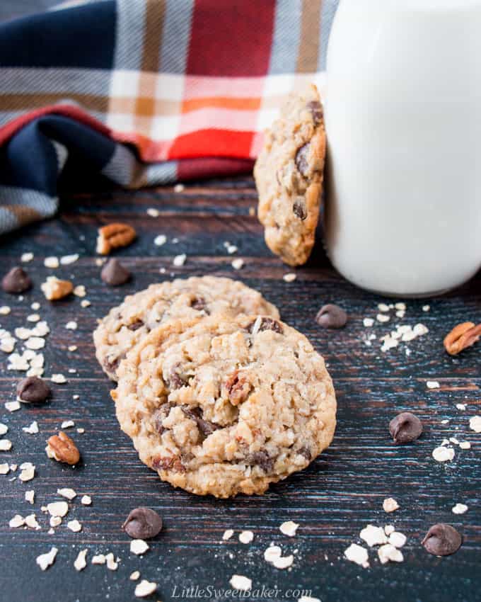 Cowboy cookies on a wooden board with a glass of milk and plaid napkin in the background.