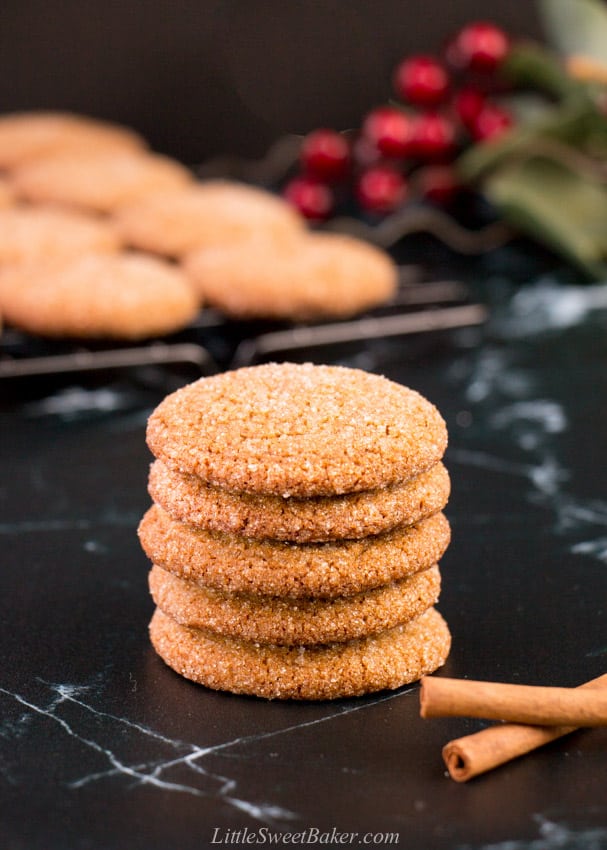 A stack of ginger snap cookies on black marble with some cinnamon sticks.