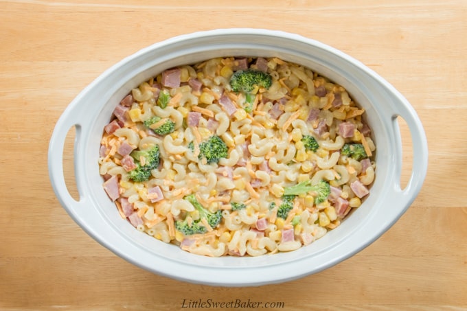 An unbaked ham and vegetable casserole in a white oval baking dish.