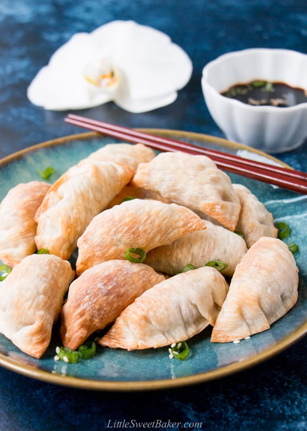 A plate of baked Chinese dumplings with dipping sauce and flower in the background.