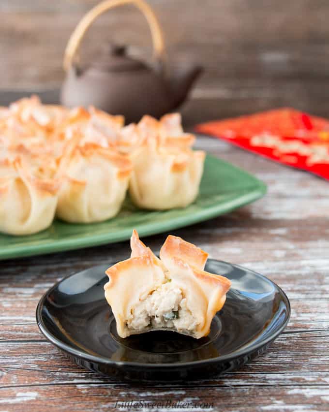 A baked turkey rangoon bitten in half with a full plate behind it.