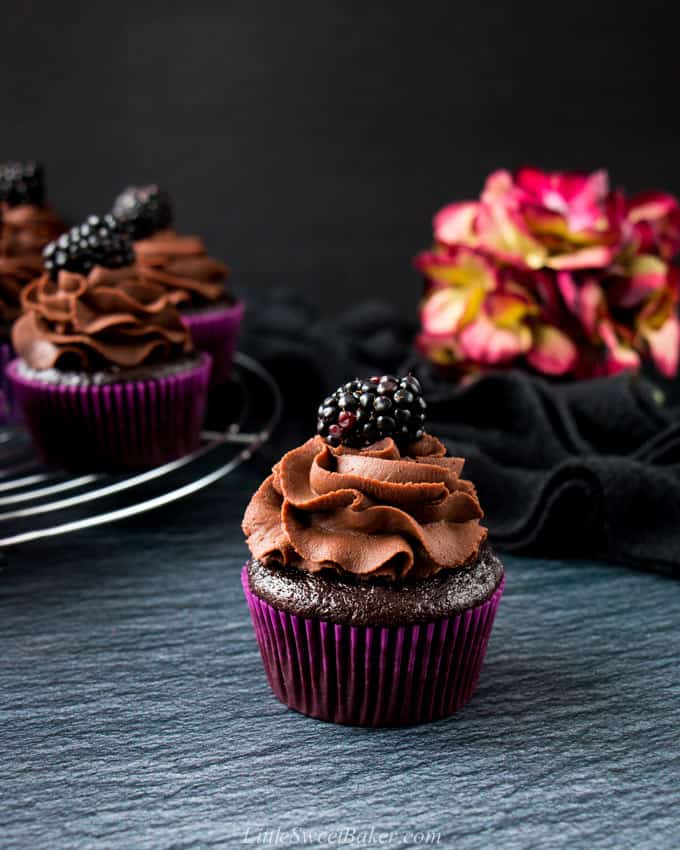 A chocolate cupcake topped with chocolate ganache and a blackberry.