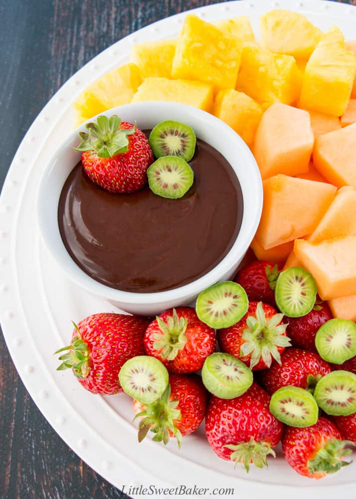 A white plate of strawberries, cantaloupe and pineapple chunks with chocolate ganache dip.