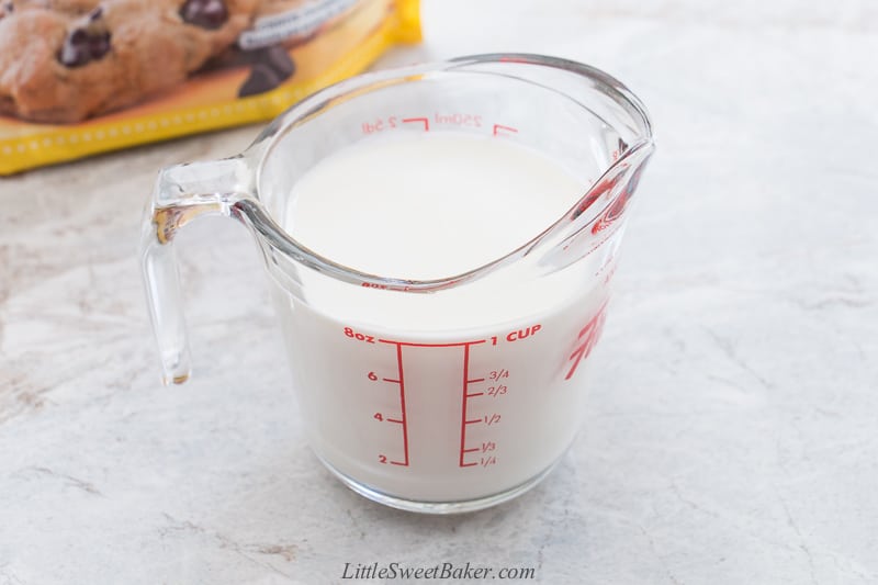 a measuring cup filled with heavy cream with a bag of chocolate chips in the background