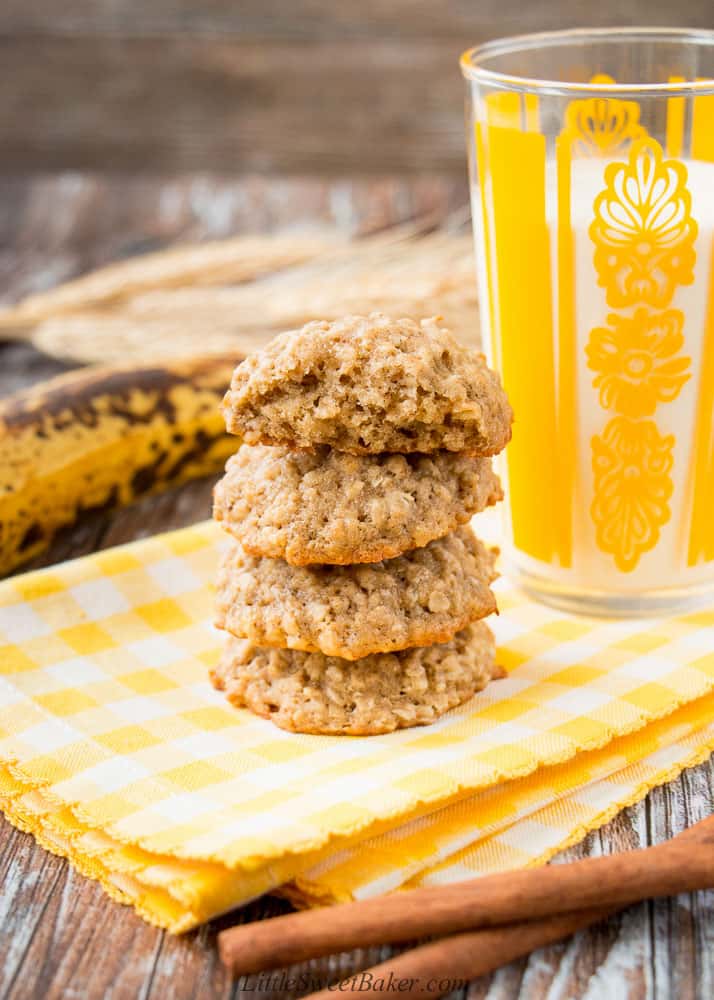 A stack of banana oatmeal cookies on a yellow napkin with a glass of milk and cinnamon sticks.