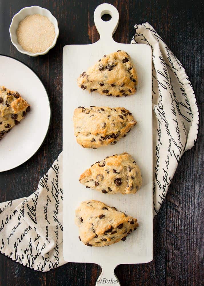 An overhead view of chocolate chip scones on a white wooden board on top of a black and cream colored napkin.