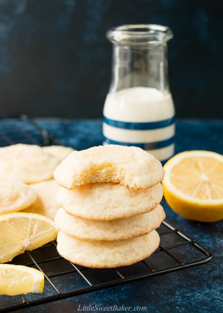 A stack of lemon sugar cookies on a cooling rack with lemons and a glass of milk.