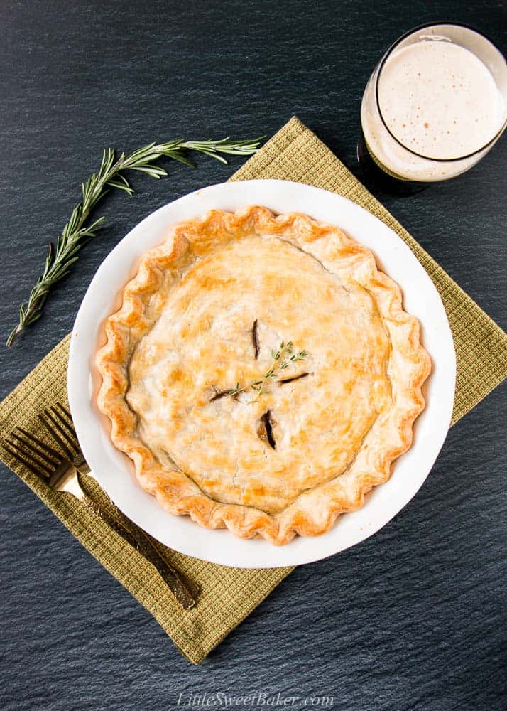 A steak and stout pie in a green kitchen towel with some gold forks, rosemary and a pint of beer.