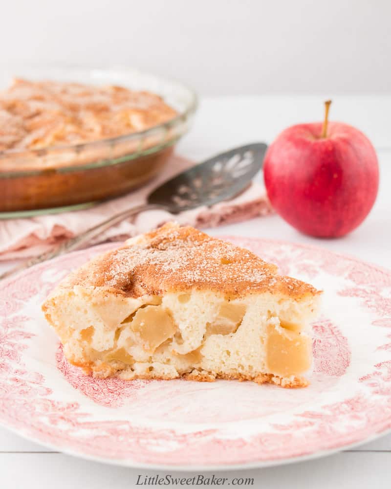 A slice of apple cinnamon cake on vintage plate with an apple and rest of cake in the background.