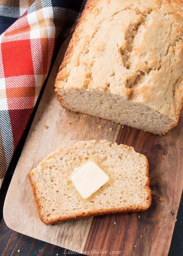 A loaf of beer bread on a cutting board with a pat of butter on a slice.