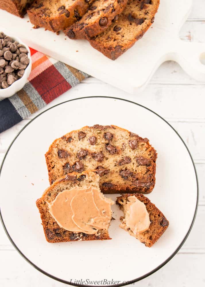 Two slices of chocolate chip banana bread on a white plate with some peanut butter on the one slice.