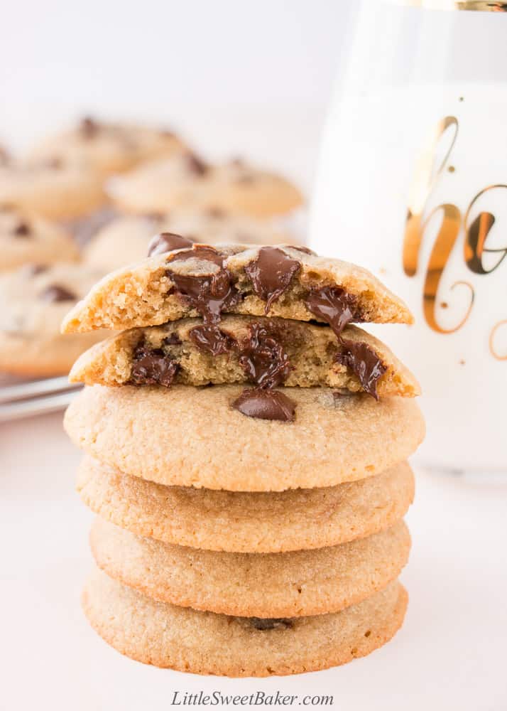 A stack of warm chocolate chip cookies with the top one broken in half.