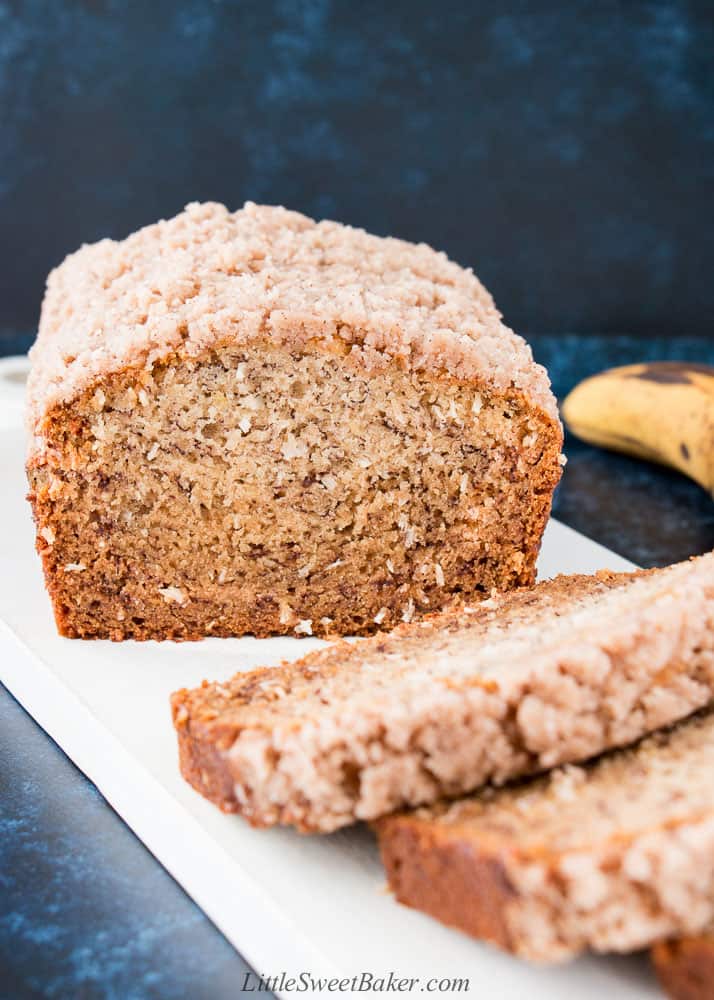 A loaf of vegan banana bread with crumb topping on a white wooden board.