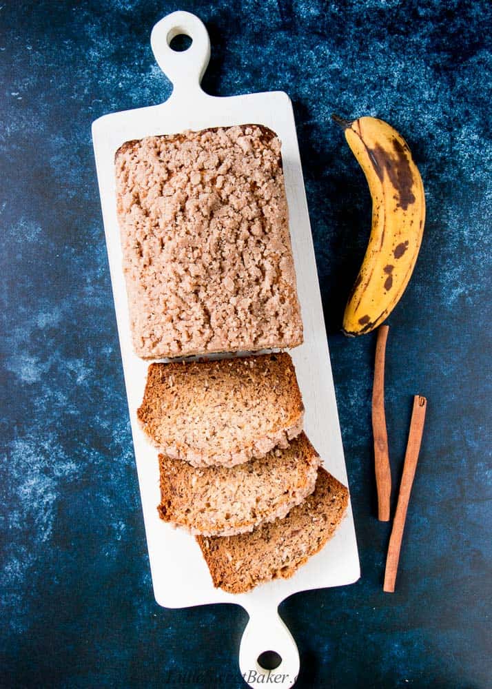 A loaf of vegan banana bread, half sliced on a white wooden cutting board.