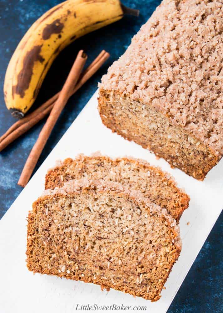 A loaf of vegan banana bread, partially sliced on a white wooden board.