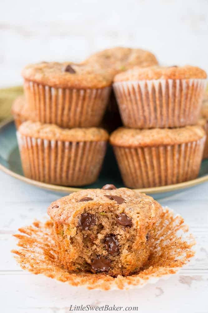 A zucchini chocolate chip muffin with a bite taken out and a plate of muffins in the background.