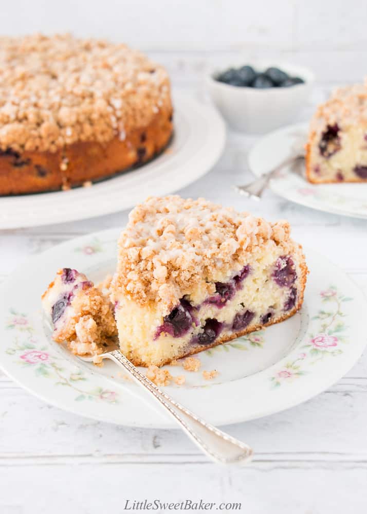 A slice of blueberry streusel cake on a white floral plate with a piece on a fork.