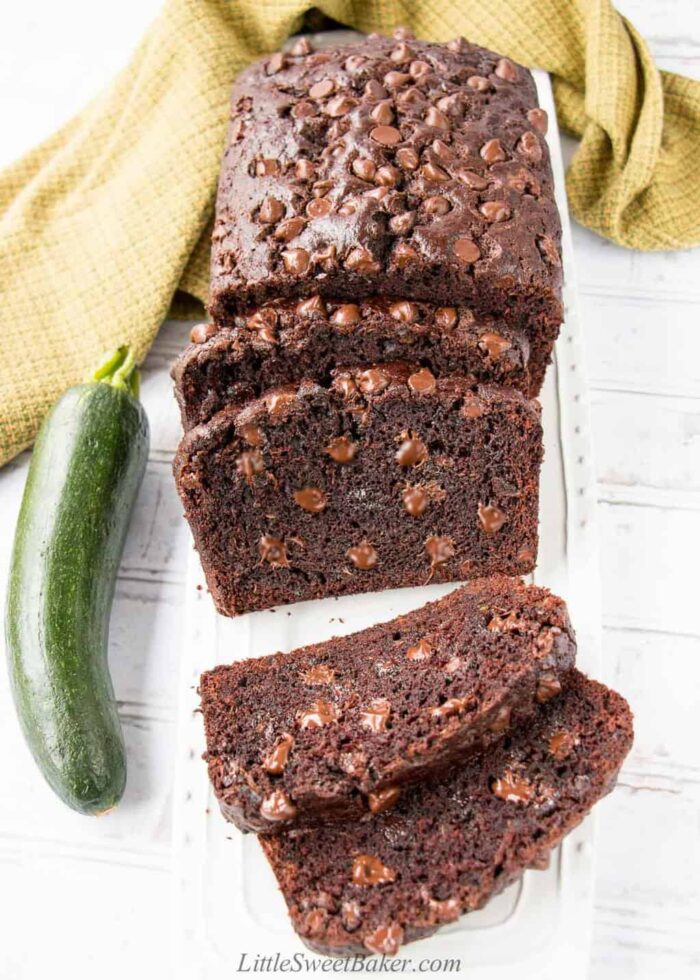 A loaf of double chocolate zucchini bread on a white platter with a few slices cut.