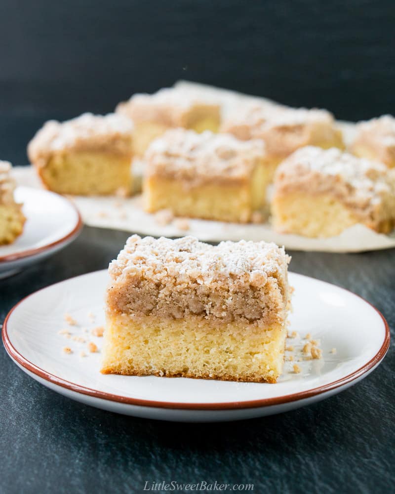 A slice of crumb cake on a plate with the rest of the cake slices in the background.