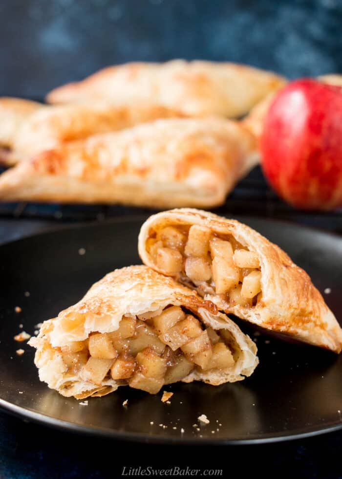 An apple turnover broken in half an a black plate to show the apple filling inside.