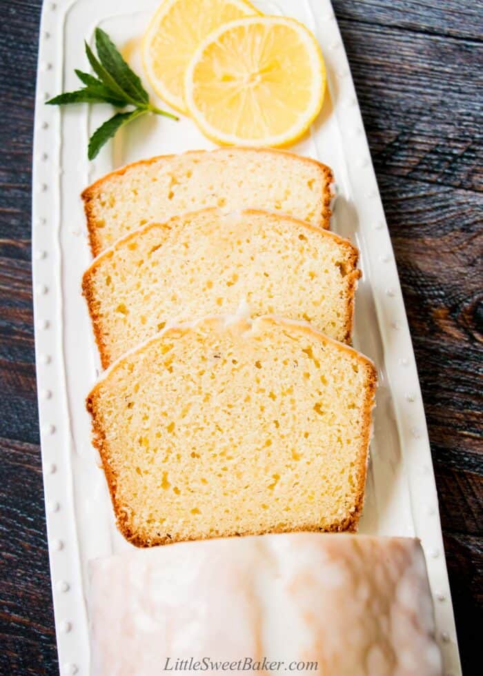 Three slices of lemon pound cake on a white serving plate with some lemon slices and mint twig.