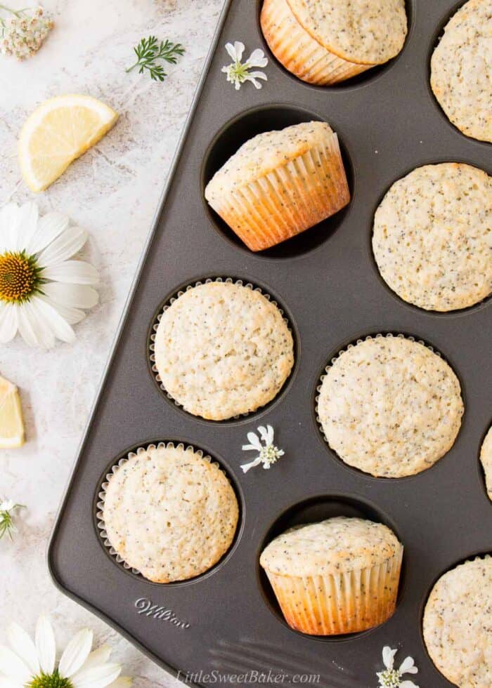 A pan of lemon poppy seed muffins on a marble surface with flowers.