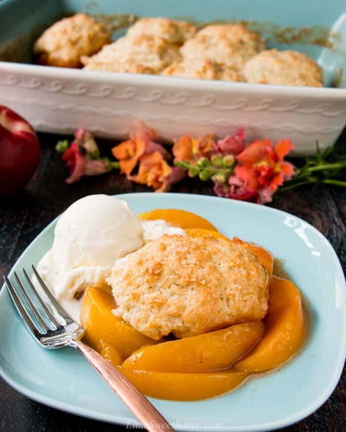 Peach cobbler with biscuits on a blue plate with ice cream.