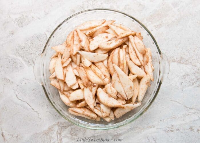 Pear slices tossed with sugar and cinnamon in a glass pie plate.