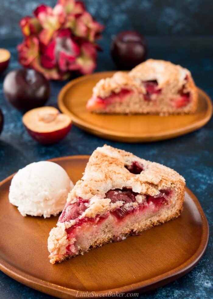 A slice of plum cake on a wooden plate with a scoop of ice cream.