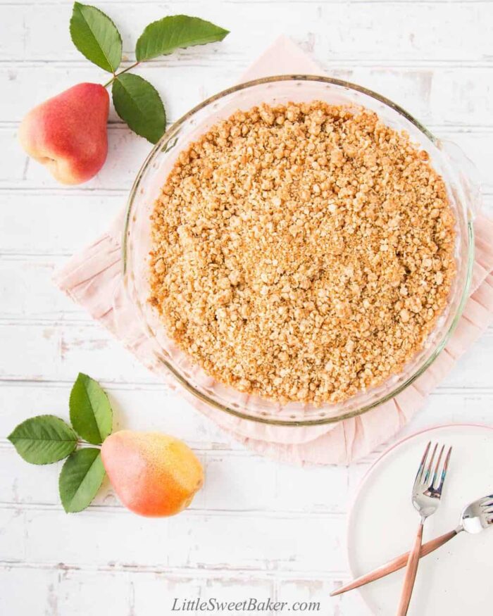 A whole plate of easy pear crisp on a pink napkin with two pears around it.