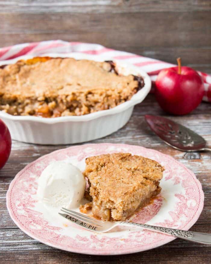 A slice of Swedish apple pie with ice cream and fork on a pink vintage looking plate.