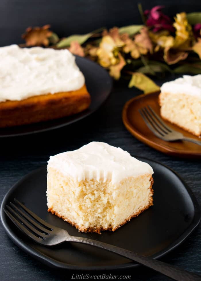 A slice of vanilla butter cake on a black plate with a piece missing.