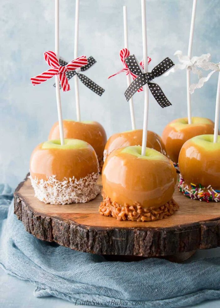 Six caramel apples on a live edge wooden board.