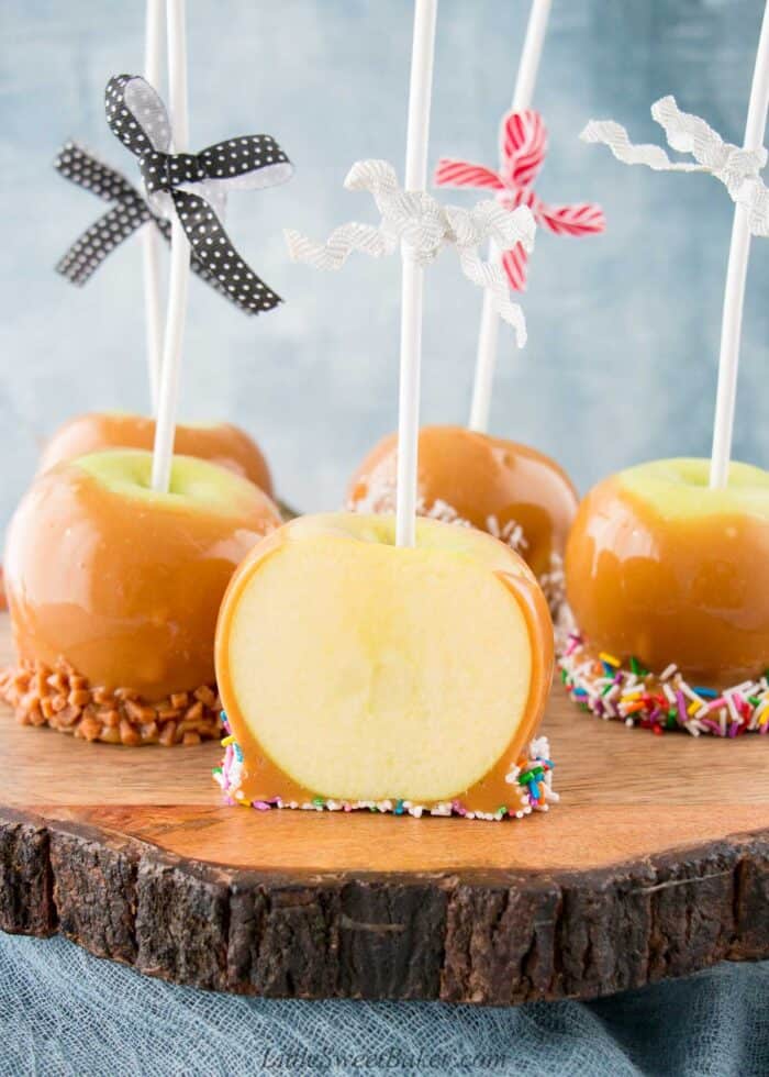 A caramel apple cut in half with four whole caramel apples behind on a wooden tray.