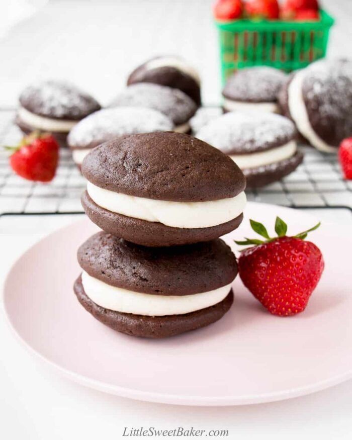 Two whoopie pies stacked on a pink plate with a strawberry.