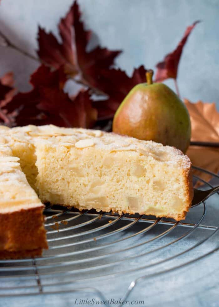 A slice of pear cake getting removed from the whole cake on a cooling rack.