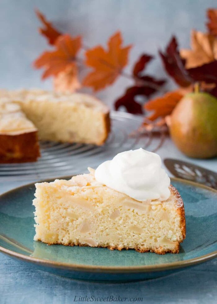 A slice of pear cake with a dollop of whipped cream on a dark teal plate.