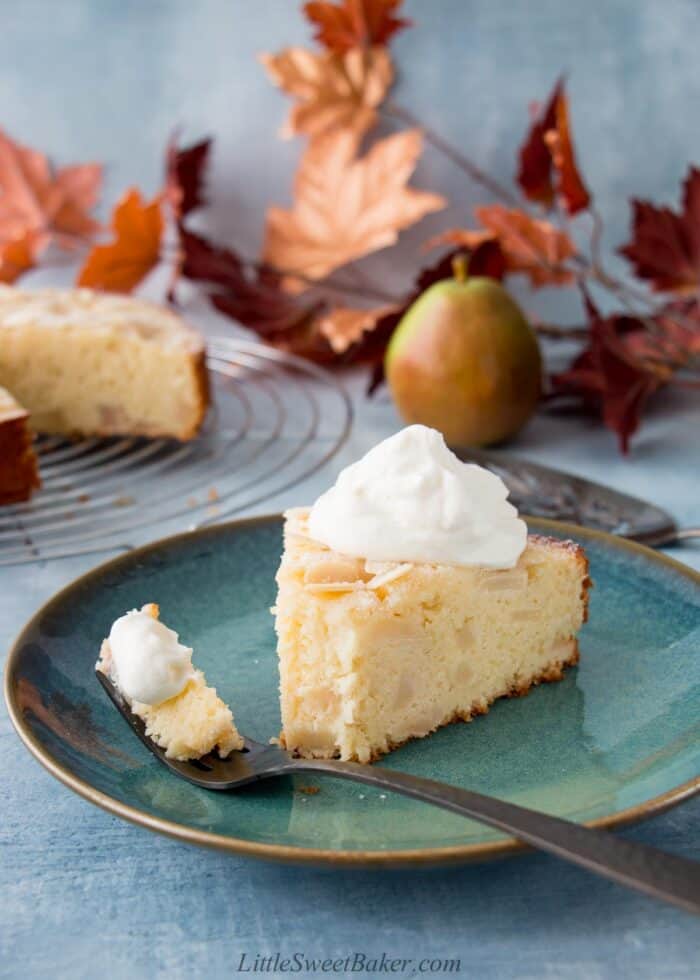 A slice of pear cake on a dark plate with a piece on a fork.