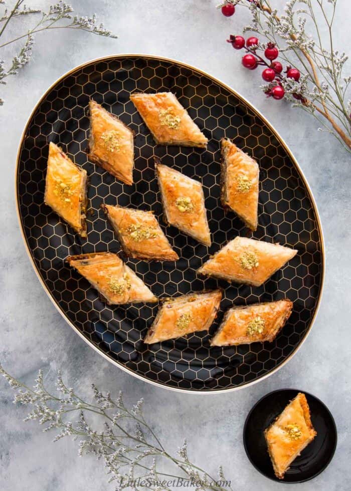 A black and gold platter of baklava topped with crushed pistachios.