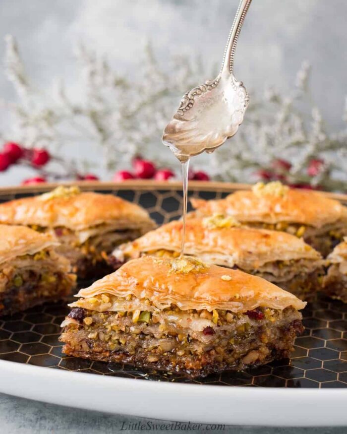 A plate of baklava made with pistachios and cranberries being drizzled with honey syrup.