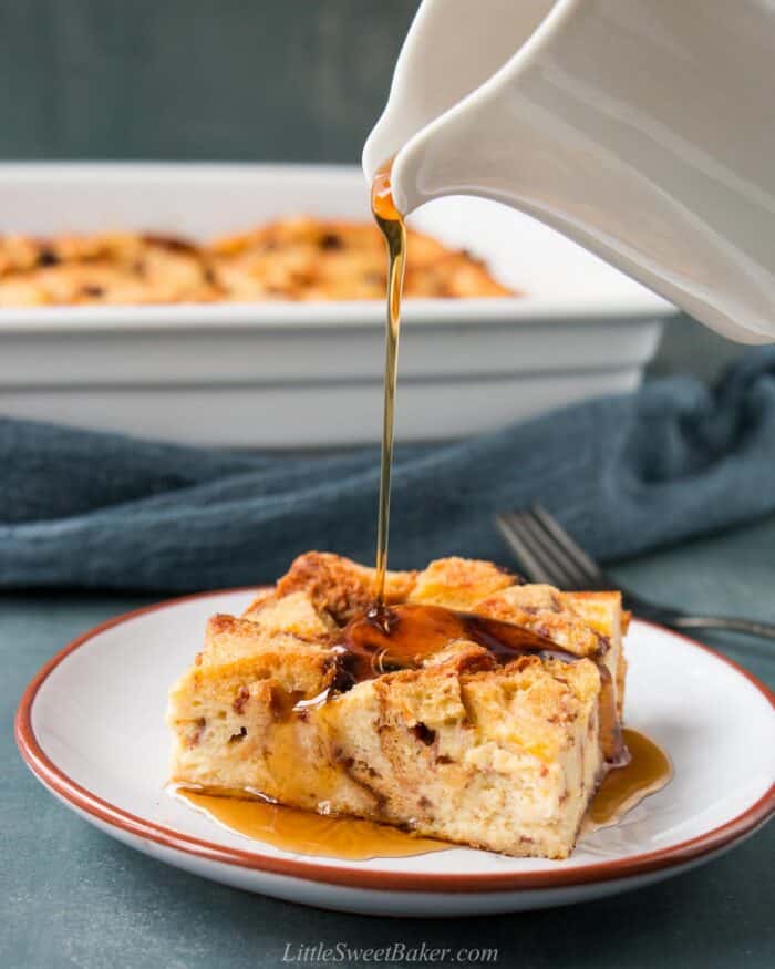 Maple syrup being poured over a slice of eggnog bread pudding.