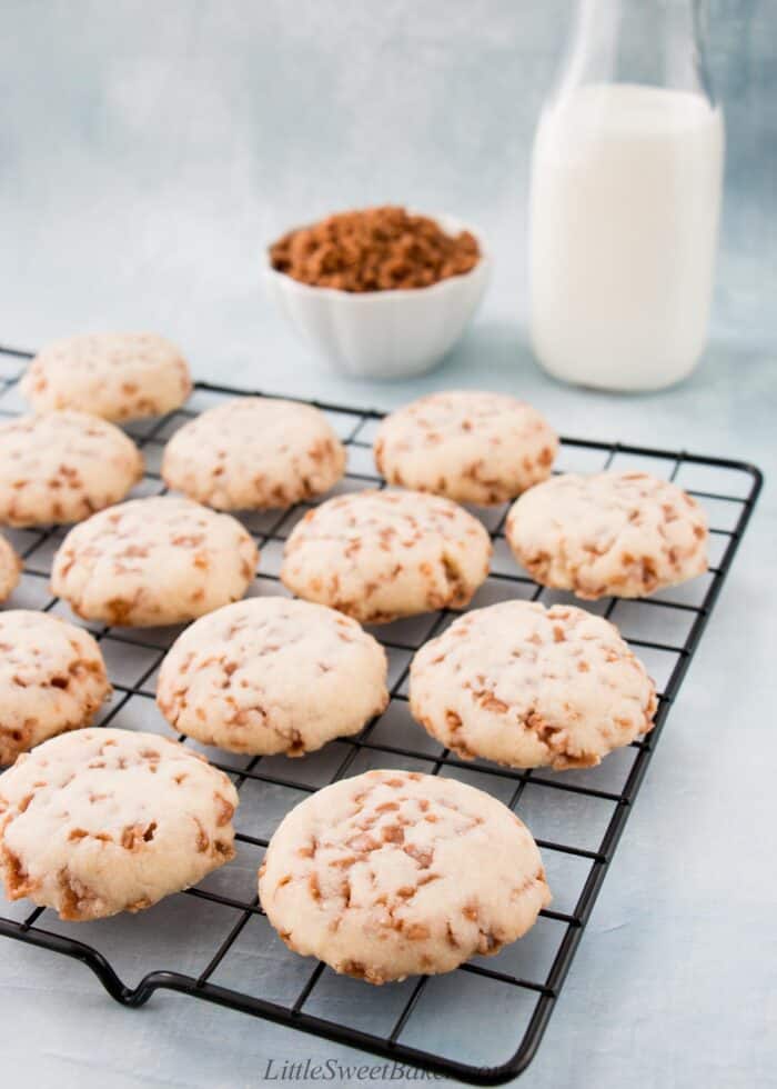 Toffee shortbread cookies on a cooling rack with a glass of milk and small bowl of Skor bits in the background.